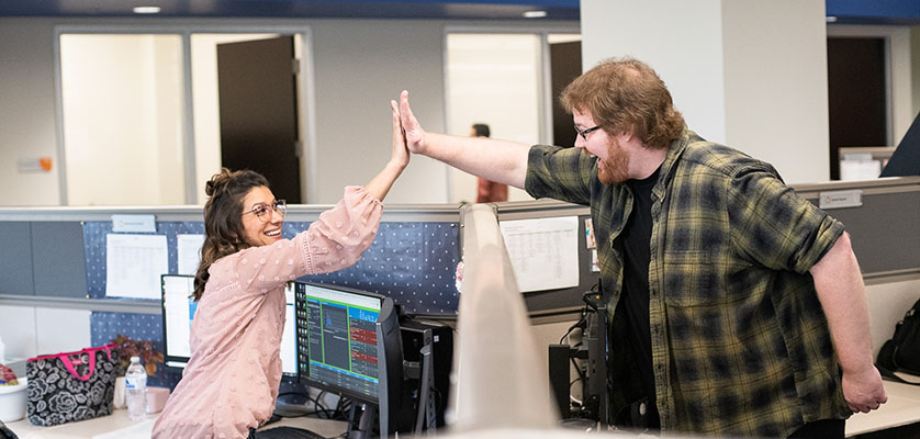 Coworkers celebrate their top workplace by high-fiving over a cubical wall