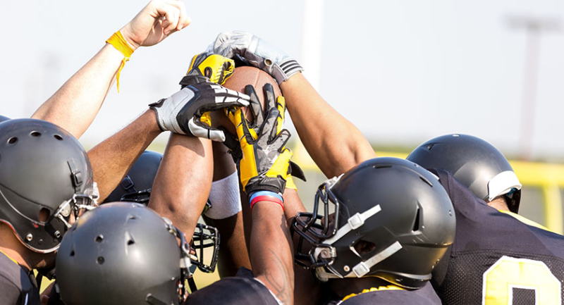 Professional football players holding ball on sidelines at stadium