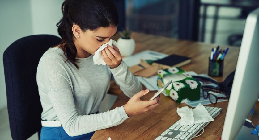 Woman staying healthy at work, blowing her nose at her desk