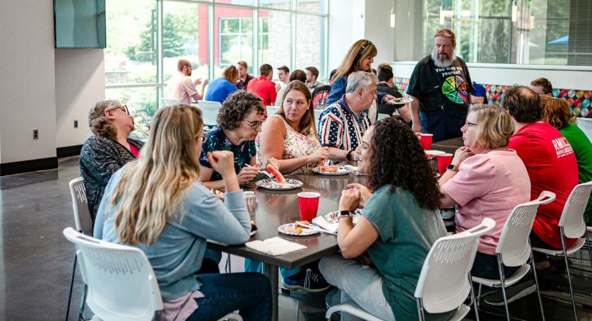 A group of people sitting down at a lunch table on their lunch break eating and talking.