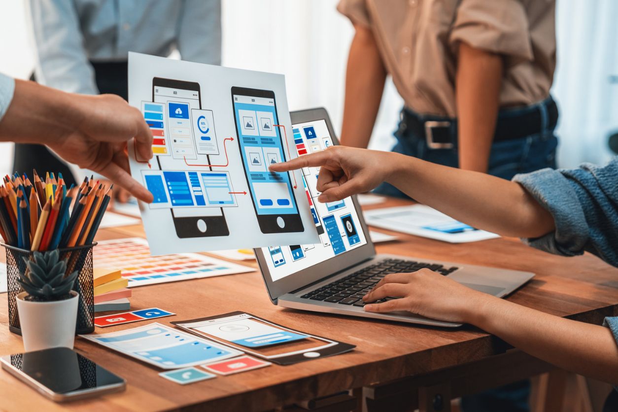 Panorama shot of front-end developer team brainstorming UI and UX designs for mobile app on paper wireframe interface. User interface development team planning for user-friendly UI design.